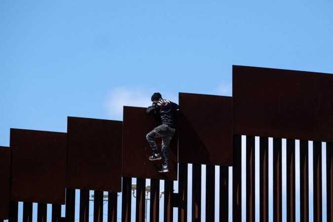 Homem escala o muro na fronteira, depois de coletar mantimentos para outros migrantes, em Tijuana 