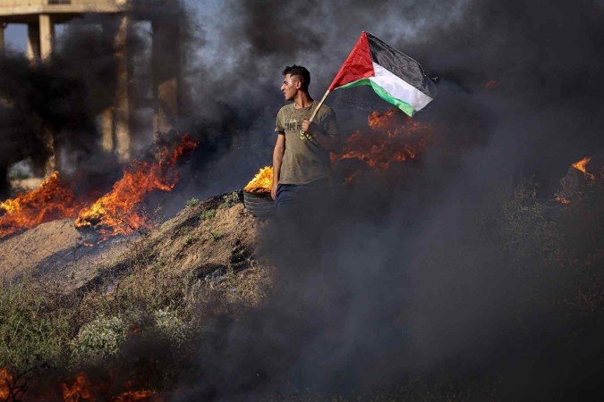 Palestino ostenta bandeira perto de pneus em chamas, em protesto a leste de Gaza 