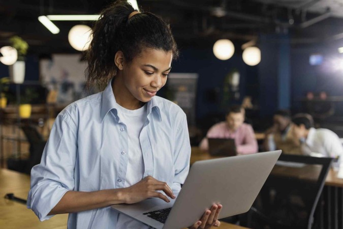 mulher sorridente segurando notebook e trabalhando -  (crédito: freepik)