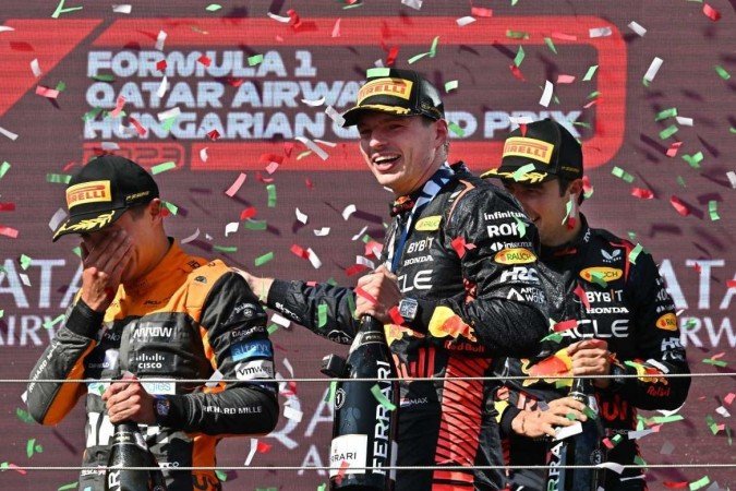 (L-R) Second placed McLaren's British driver Lando Norris, winner Red Bull Racing's Dutch driver Max Verstappen and third placed Red Bull Racing's Mexican driver Sergio Perez celebrate on the podium after the Formula One Hungarian Grand Prix at the Hungaroring race track in Mogyorod near Budapest on July 23, 2023. (Photo by ATTILA KISBENEDEK / AFP)
- (crédito: AFP) (L-R) Second placed McLaren's British driver Lando Norris, winner Red Bull Racing's Dutch driver Max Verstappen and third placed Red Bull Racing's Mexican driver Sergio Perez celebrate on the podium after the Formula One Hungarian Grand Prix at the Hungaroring race track in Mogyorod near Budapest on July 23, 2023. (Photo by ATTILA KISBENEDEK / AFP)
- (crédito: AFP)