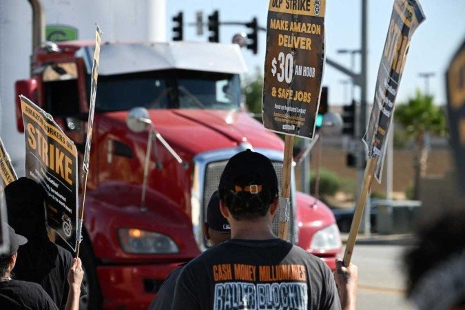 Motoristas de entrega da Amazon empregados pela empresa terceirizada Battle Tested Strategies (BTS) e Teamsters bloqueiam o tráfego de caminhões enquanto protestam do lado de fora do depósito da Amazon em Palmdale,Califórnia. - (crédito: Reprodução/ Robyn Beck / AFP) Motoristas de entrega da Amazon empregados pela empresa terceirizada Battle Tested Strategies (BTS) e Teamsters bloqueiam o tráfego de caminhões enquanto protestam do lado de fora do depósito da Amazon em Palmdale,Califórnia. - (crédito: Reprodução/ Robyn Beck / AFP)