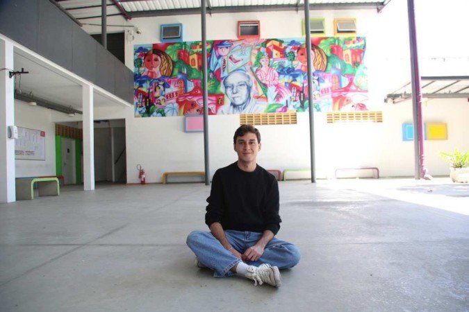 Jovem branco sorrindo sentado no chão com perna cruzada 