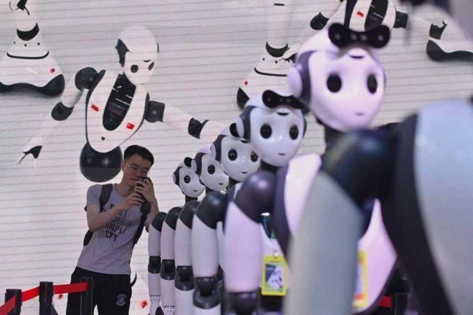 Homem tira foto de robôs durante a Conferência Mundial da Inteligência Artificial (WAIC) em Xangai, China -  (crédito: Reprodução/Wang Zhao/AFP)