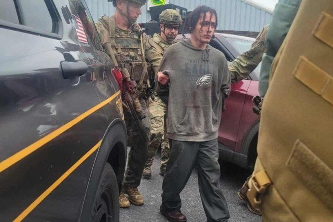 Danilo Cavalcante é condzuzido por policiais pouco depois de ser encontrado, em uma mata, por volta das 8h30 - (crédito: Pennsylvania State Police Department/AFP) Danilo Cavalcante é condzuzido por policiais pouco depois de ser encontrado, em uma mata, por volta das 8h30 - (crédito: Pennsylvania State Police Department/AFP)