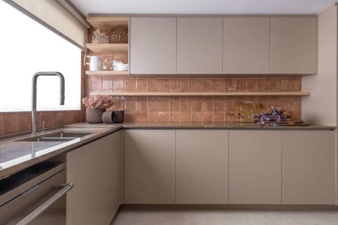 Cozinha decorada com itens de cores neutras, armários simples e com prateleiras que garantem uma organização eficiente. Materiais naturais, como a pedra da bancada e a cerâmica revestindo a parede criam um ambiente simples e funcional