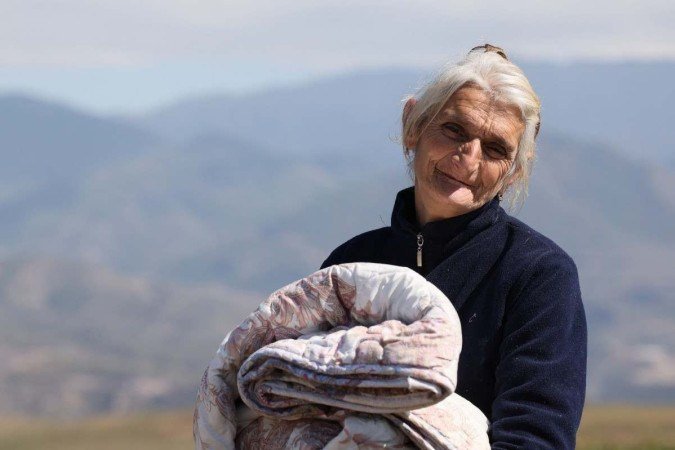 Idosa refugiada caminha pelo centro da Cruz Vermelha, perto de Kornidzor, na Armênia, com as montanhas de Karabakh ao fundo 
