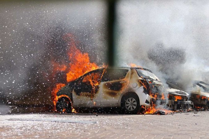 Carros são vistos em chamas após um ataque com foguetes da Faixa de Gaza em Ashkelon, sul de Israel, neste sábado (7/10)       -  (crédito: HMAD GHARABLI/AFP)