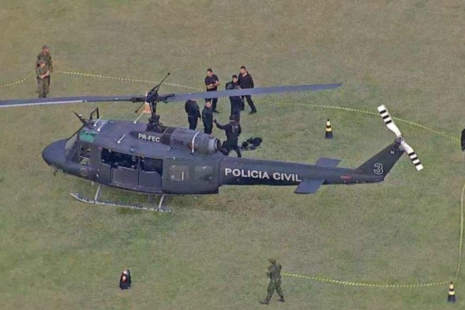Em solo, agentes cercam o helicóptero atingido e avaliam os estragos. Ação tentava capturar chefes envolvidos com a chacina de médicos - (crédito: Reprodução/TV Globo) Em solo, agentes cercam o helicóptero atingido e avaliam os estragos. Ação tentava capturar chefes envolvidos com a chacina de médicos - (crédito: Reprodução/TV Globo)