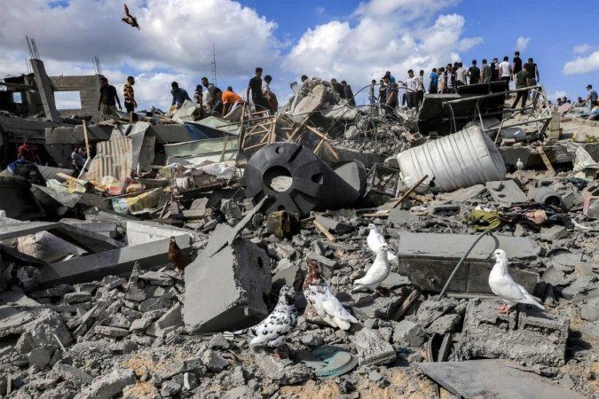 Pombos pousam nos escombros enquanto pessoas inspecionam os restos de um edifício destruído após o bombardeio israelense em Khan Yunis, no sul da Faixa de Gaza, nesta quarta-feira (18/10). Há pelo menos 40 feridos e sete mortos - (crédito: Mahmud HAMS / AFP) Pombos pousam nos escombros enquanto pessoas inspecionam os restos de um edifício destruído após o bombardeio israelense em Khan Yunis, no sul da Faixa de Gaza, nesta quarta-feira (18/10). Há pelo menos 40 feridos e sete mortos - (crédito: Mahmud HAMS / AFP)