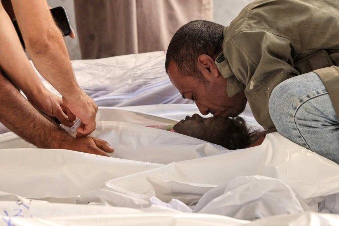 Avô beija corpo de menina palestina atingida por bombardeio israelense, em Rafah, no sul de Gaza 