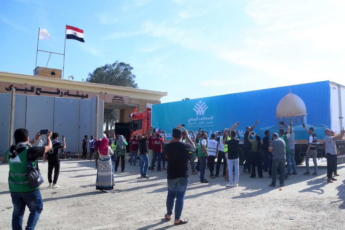 Pessoas no lado egípcio da passagem de fronteira de Rafah observam enquanto um comboio de caminhões transportando ajuda humanitária cruza para a Faixa de Gaza       