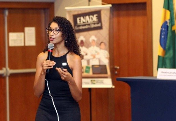 Mulher negra de vestido preto fala ao microfone.
