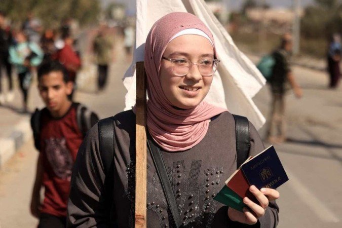 Uma mulher carrega um passaporte ucraniano ao lado de outros com uma bandeira branca, enquanto palestinos que fogem da Cidade de Gaza em direção às áreas do sul caminham por uma estrada em 7 de novembro de 2023, em meio às batalhas em curso entre Israel e o grupo islâmico palestino Hamas.  -  (crédito: MAHMUD HAMS / AFP)