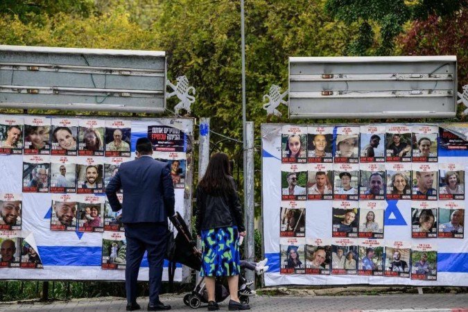 Imagem mostra um casal com filhos olha retratos de reféns israelenses mantidos em Gaza desde o ataque de 7 de outubro por militantes do Hamas, em outdoors em Jerusalém. -  (crédito: John MACDOUGALL / AFP)