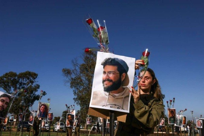 Soldado israelense deposita flor sobre fotografia de vítima do massacre de 7 de outubro, durante a festa rave no kibbutz de Re'im