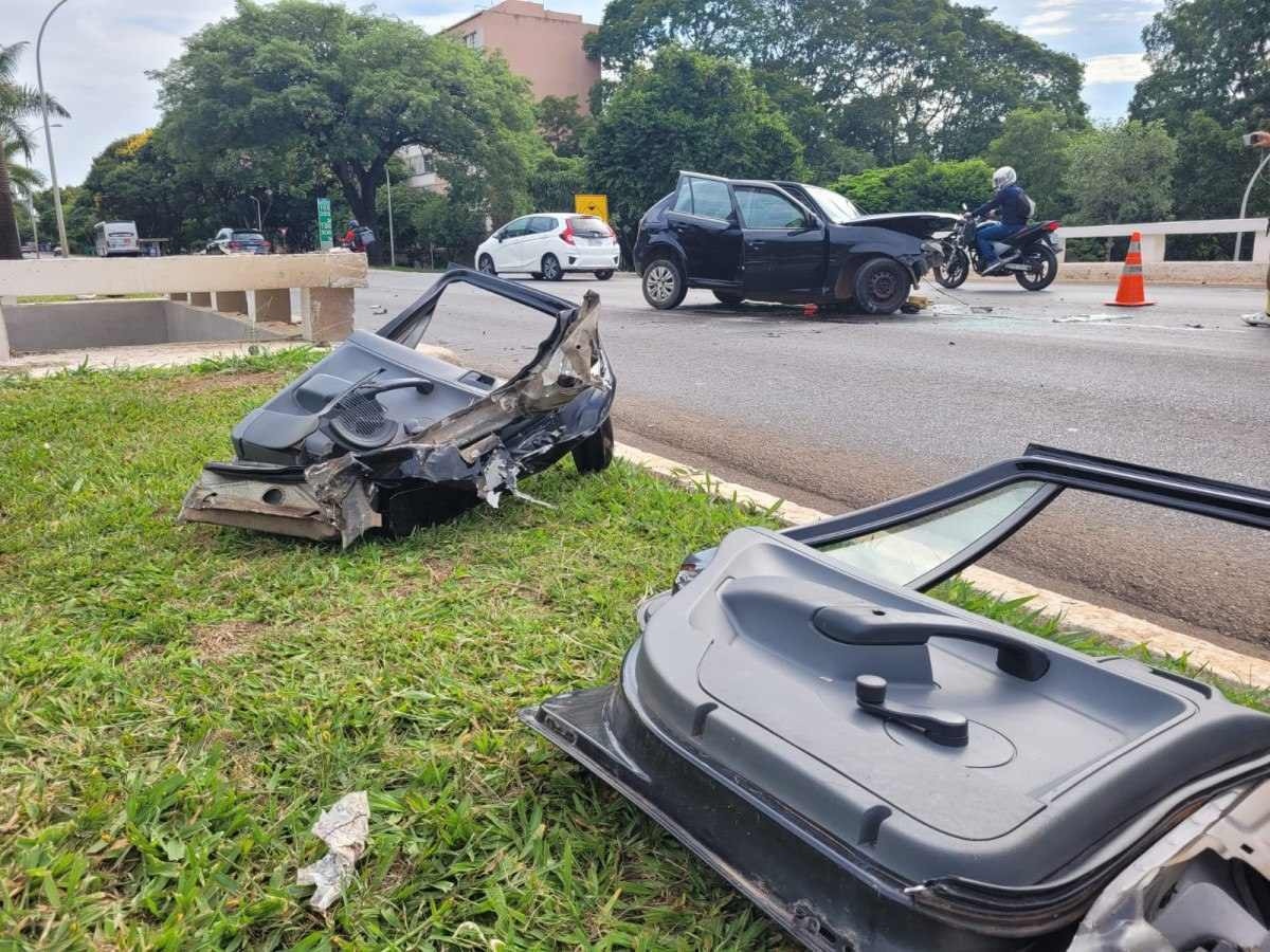 Duas portas no chão após Gol preto colidir com mureta de proteção do Eixinho Sul