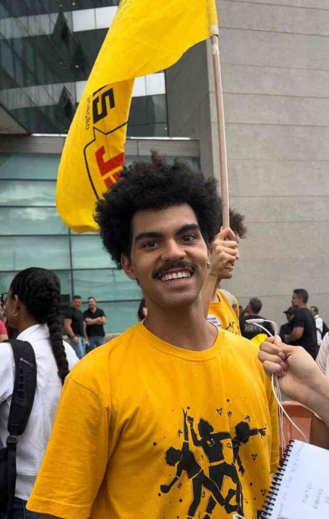 Maktus Fabiano, estudante da Universidade de Brasília. Jovem negro, de cabelos afro e bigode preto usando uma camiseta amarela.