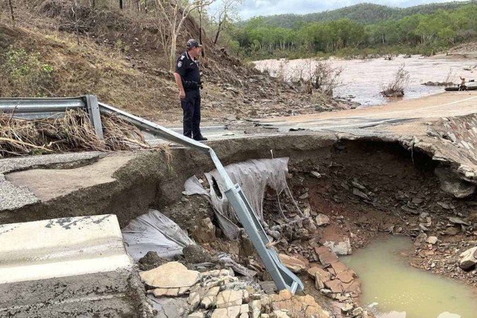 Policial parado em uma parte danificada da rodovia Mulligan, perto da cidade de Cooktown, no norte da Austrália, depois que fortes chuvas causaram grandes inundações repentinas - (crédito: HANDOUT / QUEENSLAND POLICE SERVICE / AFP) Policial parado em uma parte danificada da rodovia Mulligan, perto da cidade de Cooktown, no norte da Austrália, depois que fortes chuvas causaram grandes inundações repentinas - (crédito: HANDOUT / QUEENSLAND POLICE SERVICE / AFP)