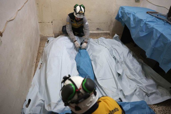 Voluntários da Defesa Civil Síria, conhecidos como Capacetes Brancos, depositam os corpos de vítimas da mesma família em um hospital após ataques aéreos russos noturnos perto da cidade de Armanaz       -  (crédito: OMAR HAJ KADOUR / AFP)
