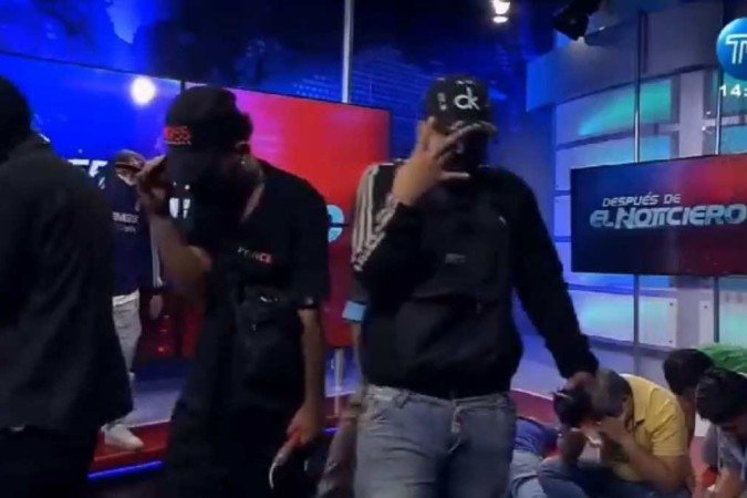 Ao fundo, funcionários do canal de televisão são vistos rendidos, com a cabeça abaixada, no chão 
