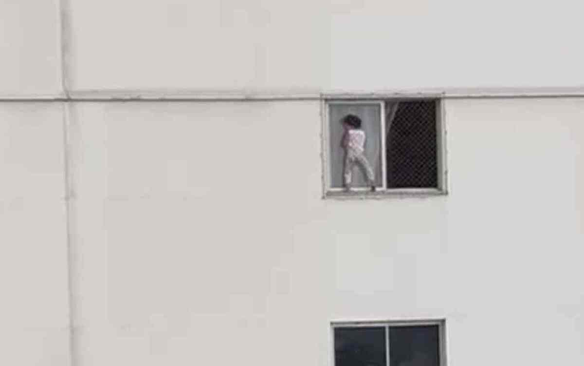 Criança brinca entre janela e a tela de proteção em apartamento do 4º andar