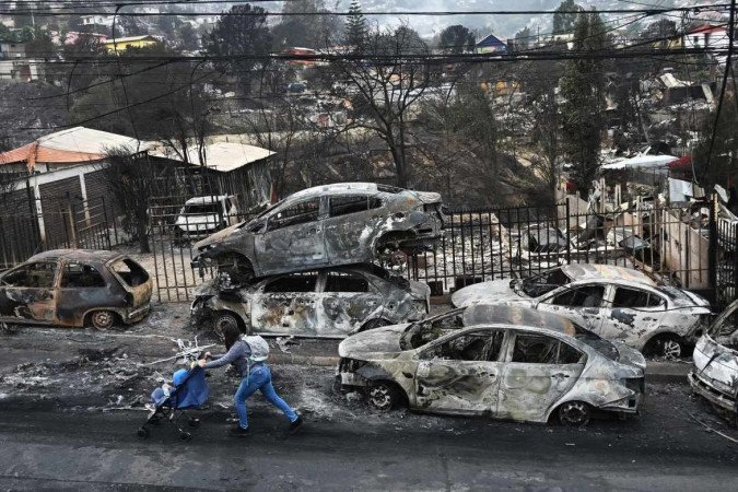 Moradora empurra carrinho com bebê diante de carros carbonizados 