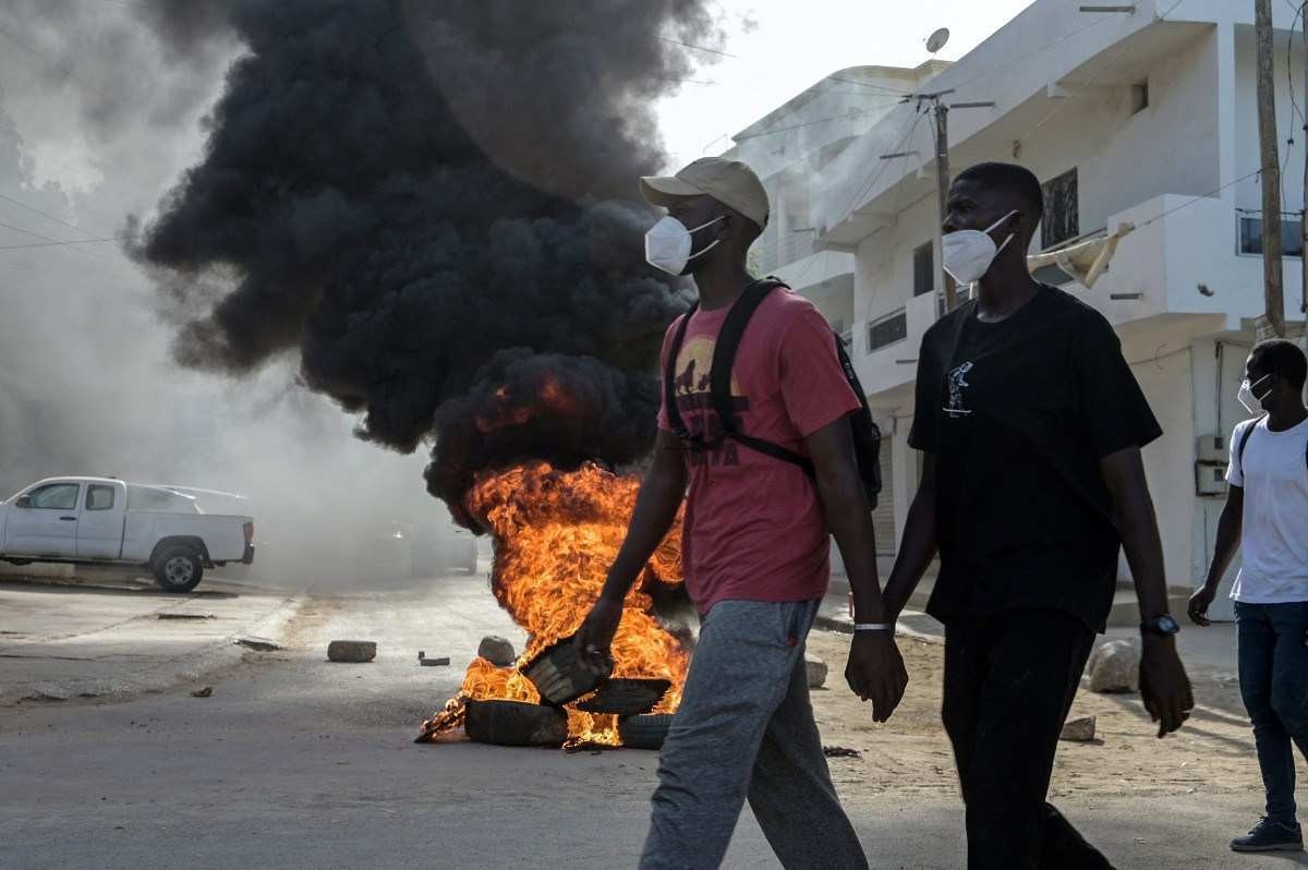 Manifestantes caminham ao lado de uma barricada em chamas durante manifestações convocadas pelos partidos da oposição em Dakar, em 4 de fevereiro de 2024     