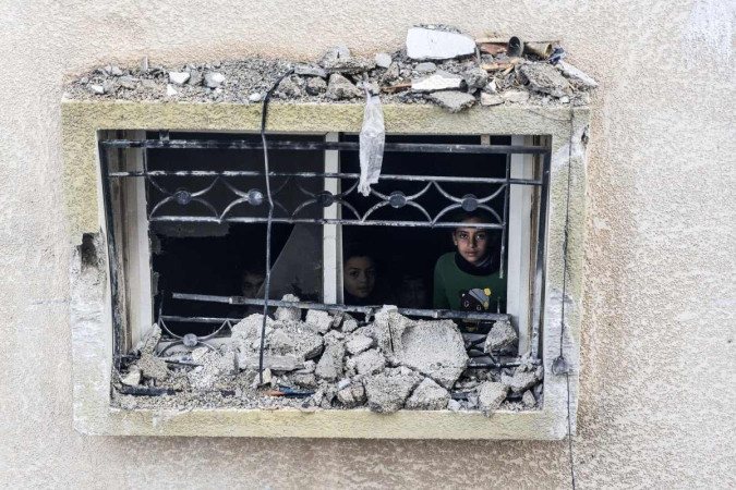 Crianças olham pela janela de um prédio danificado, após bombardeio israelense em Rafah  -  (crédito: Mahmud Hams/AFP)