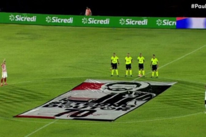 Jogadores do Botafogo-SP e do Corinthians erguem os braços diante do bandeirão em memória do ídolo  -  (crédito: Foto: Reprodução TV Record)