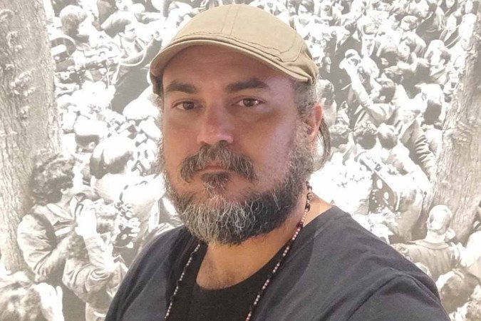 Paulo Wesley Pinheiro foi o único doutor da Universidade de Brasília a ser nomeado para a última edição do prêmio, com pesquisa sobre desigualdades sociais Homem branco de barba grisalha e boina bege posa em frente à fotografia em preto e branco de uma multidão