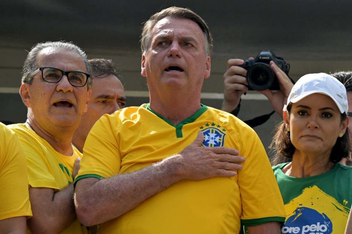  Former Brazilian President Jair Bolsonaro (C) sings the national anthem next to his wife Michelle Bolsonaro (R) and Pastor Silas Malafaia (L) during a rally in Sao Paulo, Brazil, on February 25, 2024, to reject claims he plotted a coup with allies to remain in power after his failed 2022 reelection bid. Investigators say the far-right ex-army captain led a plot to falsely discredit the Brazilian election system and prevent the winner of the vote, leftist President Luiz Inacio Lula da Silva, from taking power. A week after Lula took office on January 1, 2023, thousands of Bolsonaro supporters stormed the presidential palace, Congress and Supreme Court, urging the military to intervene to overturn what they called a stolen election. (Photo by NELSON ALMEIDA / AFP)       