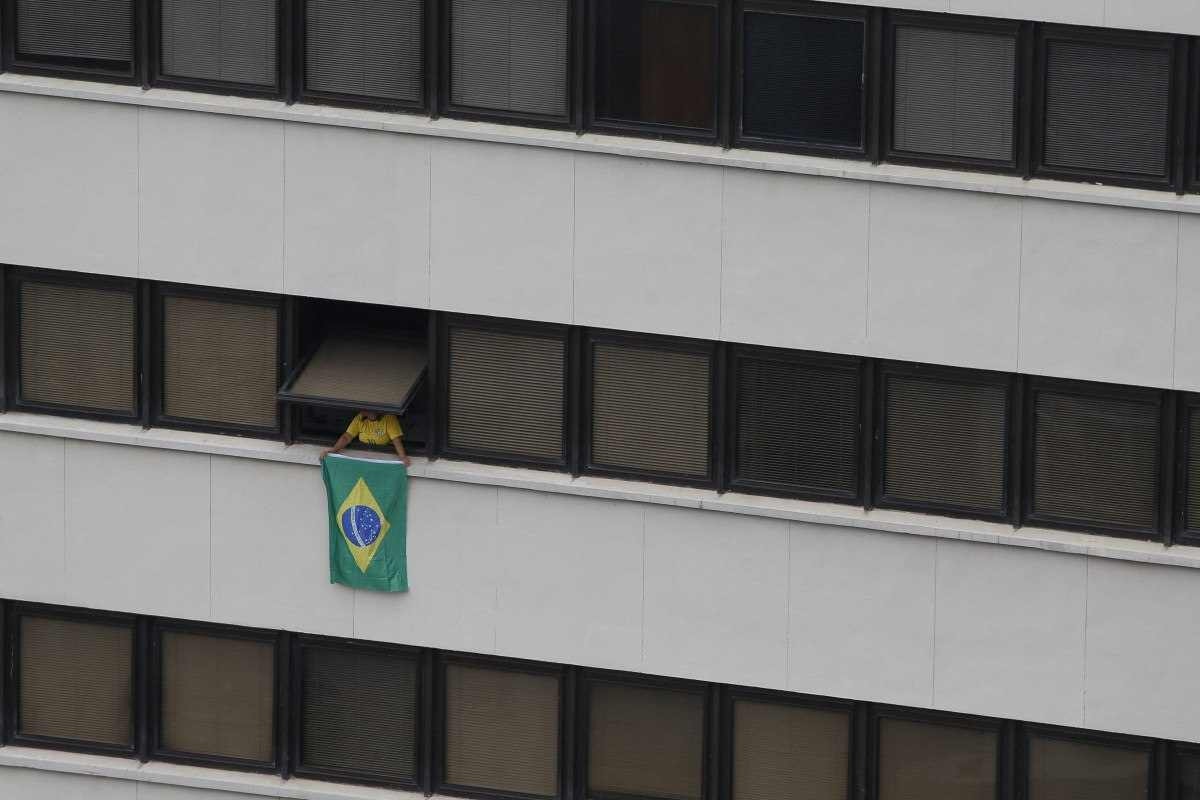  A supporter of former Brazilian President Jair Bolsonaro (2019-2022) looks out the window of a building holding a Brazilian flag during a rally in Sao Paulo, Brazil, on February 25, 2024, to reject claims he plotted a coup with allies to remain in power after his failed 2022 reelection bid. Investigators say the far-right ex-army captain led a plot to falsely discredit the Brazilian election system and prevent the winner of the vote, leftist President Luiz Inacio Lula da Silva, from taking power. A week after Lula took office on January 1, 2023, thousands of Bolsonaro supporters stormed the presidential palace, Congress and Supreme Court, urging the military to intervene to overturn what they called a stolen election. (Photo by Miguel SCHINCARIOL / AFP)       