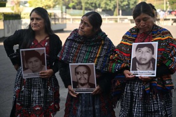 Parentes seguram retratos de três vítimas de um despejo rodoviário realizado pelos militares em 2012, durante uma cerimônia maia em frente ao Palácio da Justiça na Cidade da Guatemala       -  (crédito: JOHAN ORDONEZ / AFP)