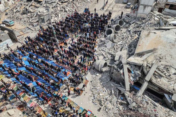  In this aerial view, Palestinians attend the Friday noon prayers in front of the ruins of the al-Faruq mosque, destroyed in Israeli strikes in Rafah in the southern Gaza Strip on March 1, 2024, amid continuing battles between Israel and the Palestinian militant group Hamas. (Photo by SAID KHATIB / AFP)
      Caption  -  (crédito:  AFP)