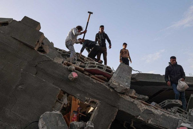 Homens palestinos vasculham os escombros da casa da família destruída num ataque aéreo israelense noturno em Rafah - (crédito: SAID KHATIB / AFP) Homens palestinos vasculham os escombros da casa da família destruída num ataque aéreo israelense noturno em Rafah - (crédito: SAID KHATIB / AFP)