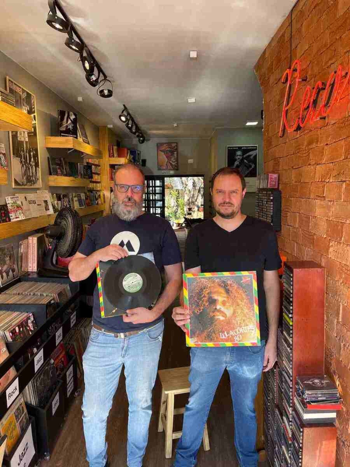João (óculos e barba) e Gustavo segurando o disco mais raro do Brasil, "Rosa de Sangue", de Lula Côrtes