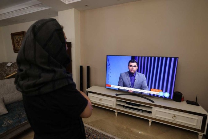 
Uma mulher iraniana assiste a um canal de TV iraniano, que cobre as notícias do ataque do Irã a Israel, em 14 de abril de 2024 -  (crédito: ATTA KENARE / AFP)