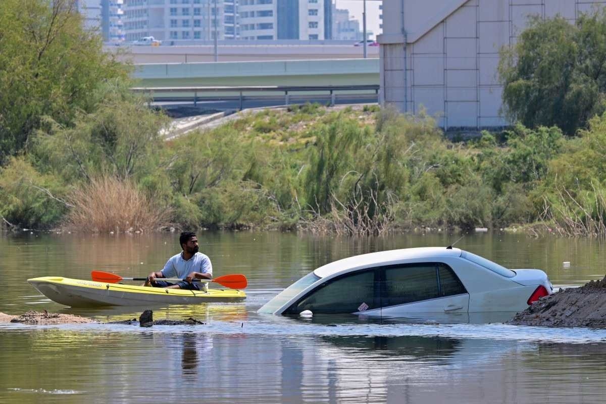  A man steers his canoe past a stranded car on a flooded street in Dubai following heavy rains on April 18, 2024. Dubais giant highways were clogged by flooding and its major airport was in chaos as the Middle East financial centre remained gridlocked on April 18, a day after the heaviest rains on record. (Photo by Giuseppe CACACE / AFP)       