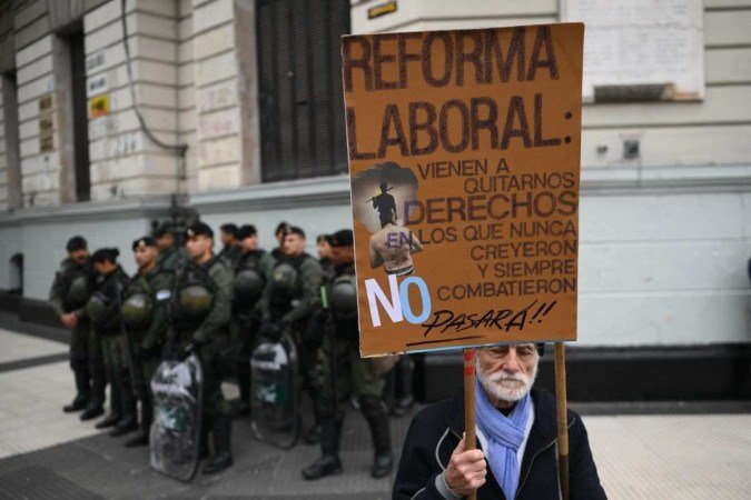  A man holds a placard against labor reform next to riot police as members of labor and social organizations march during a May Day (Labor Day) demonstration in Buenos Aires on May 1, 2024. (Photo by Luis ROBAYO / AFP)
      Caption 