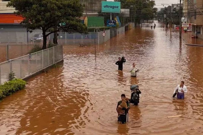 Chuvas no RS: pessoas tentam atravessar ruas alagadas no bairro Navegantes, em Porto Alegre  -  (crédito: Carlos Fabal/AFP)