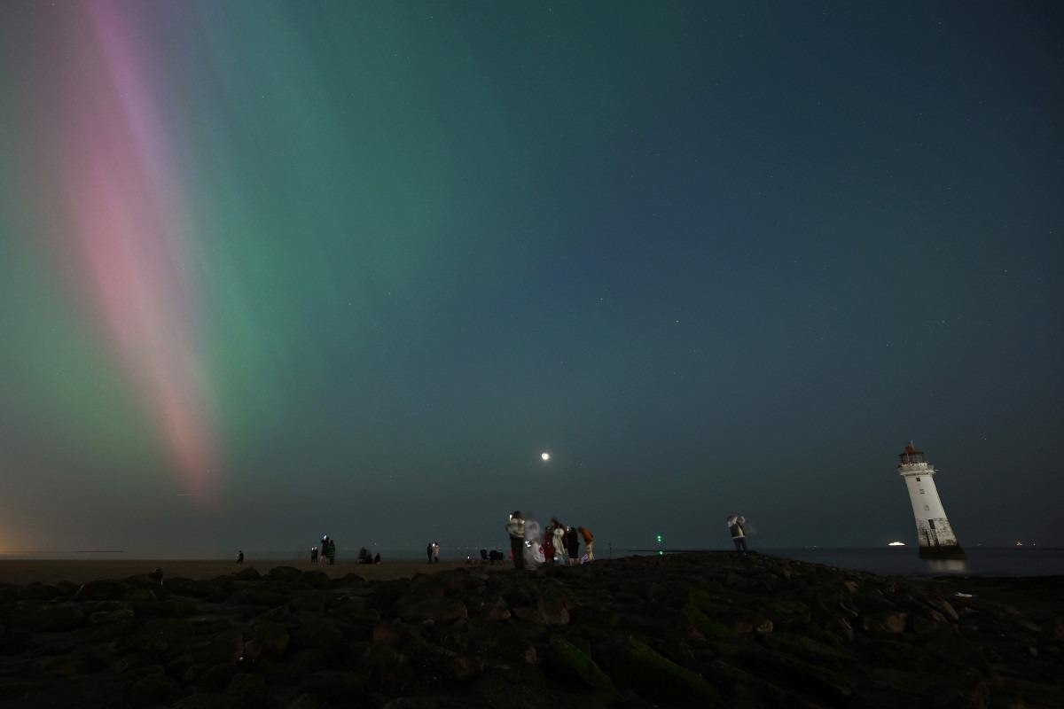 As pessoas se reúnem para observar a Aurora Boreal em New Brighton, no noroeste da Inglaterra, no final de 10 de maio de 2024.