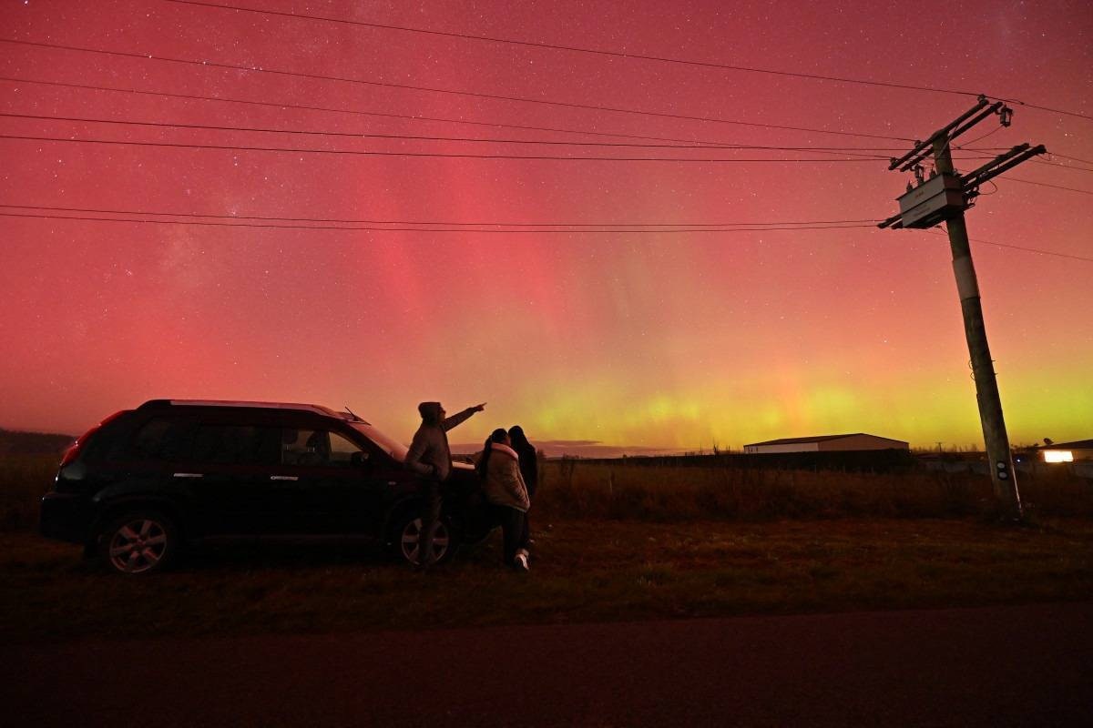 As pessoas olham para a Aurora Australis, também conhecida como Luzes do Sul, nos arredores de Rolleston, em Christchurch, em 11 de maio de 2024