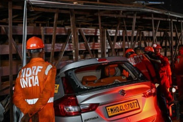 Pessoal da Força Nacional de Resposta a Desastres (NDRF) inspeciona um carro fortemente danificado no local onde um outdoor desabou em um posto de gasolina após uma tempestade de poeira em Mumbai em 13 de maio de 2024 -  (crédito: Punit PARANJPE / AFP)