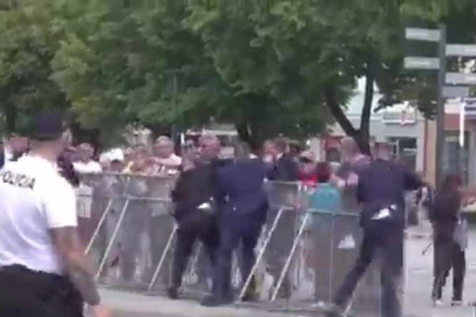 O chefe de governo (C, de terno preto) é atingido 
à queima-roupa; pouco depois, tomba no chão