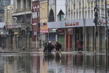 Pessoas caminham por rua inundada: risco de infecção -  (crédito: NELSON ALMEIDA / AFP)