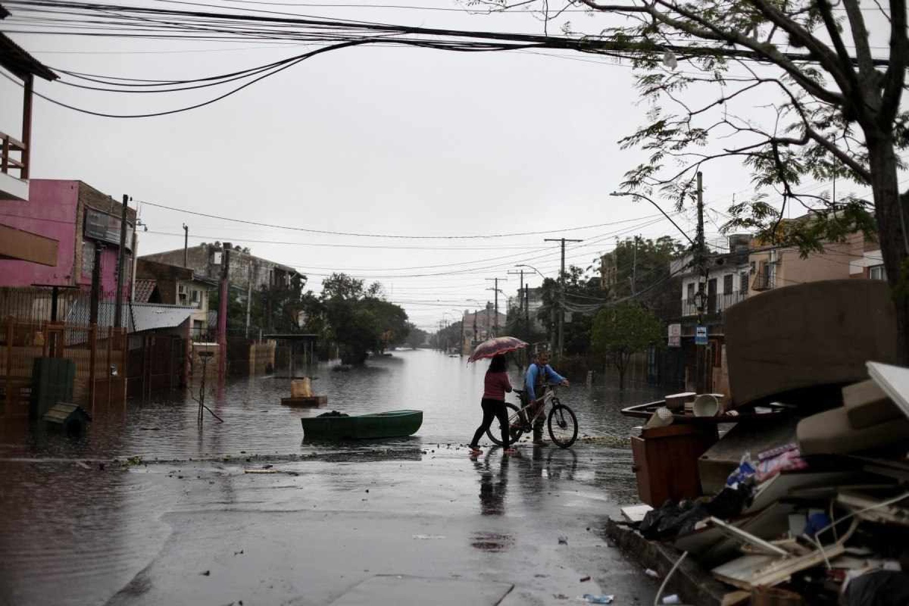  A couple walks on a partially flooded street in the Sarandi neighborhood, one of the hardest hit by the heavy rains in Porto Alegre, Rio Grande do Sul state, Brazil, on May 27, 2024. Cities and rural areas alike in Rio Grande do Sul have been hit for weeks by an unprecedented climate disaster of torrential rains and deadly flooding. More than half a million people have fled their homes, and authorities have been unable to fully assess the extent of the damage. (Photo by Anselmo Cunha / AFP)       Caption 