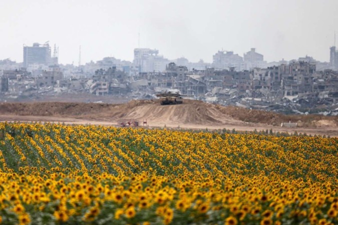 Tanque do Exército israelense se movimenta entre plantação de girassóis, no lado israelense da fronteira, e a devastação em Gaza  -  (crédito: Menahem Kahana/AFP)