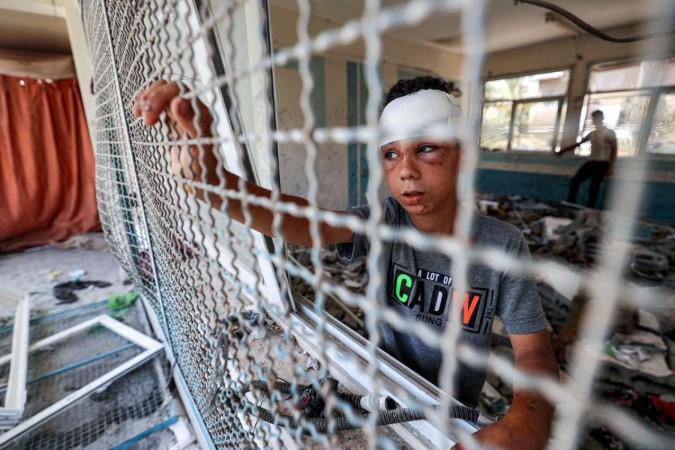 Garoto ferido é fotografado em janela de sala de aula destruída em escola mantida pela UNRWA, em Nuseirat  -  (crédito: Eyad Baba/AFP)