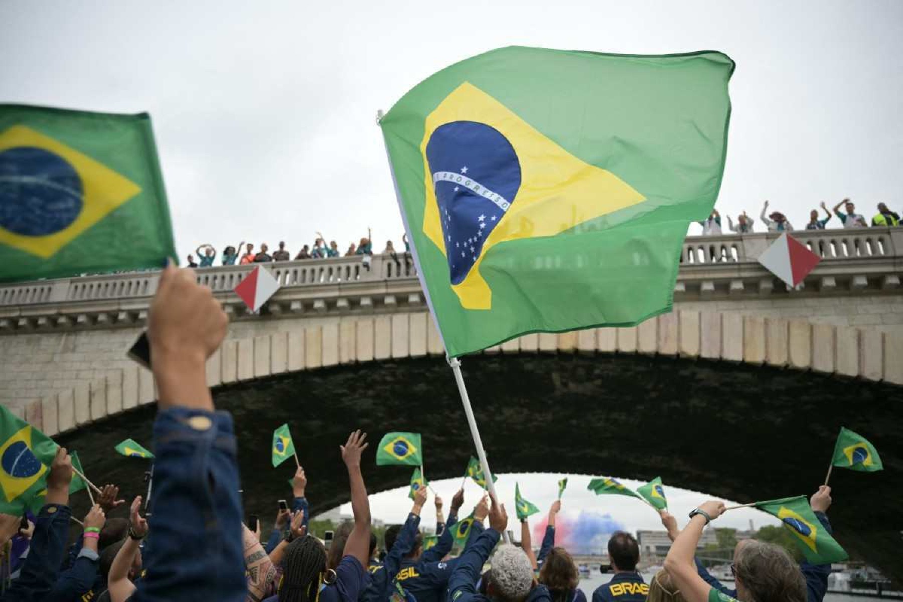 Atletas da delegação brasileira comemoram agitando bandeiras brasileiras enquanto navegam em um barco pelo rio Sena durante a cerimônia de abertura dos Jogos Olímpicos de Paris 2024, em Paris