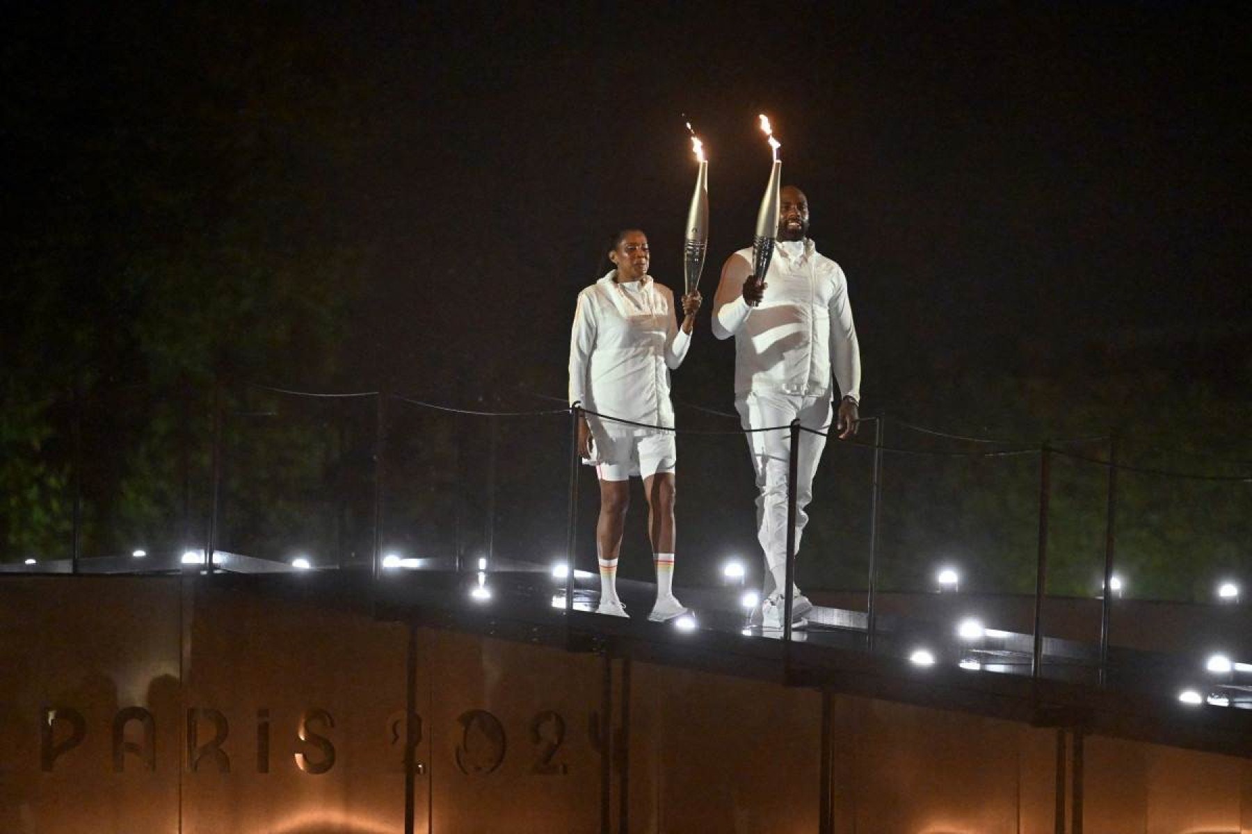 Os portadores da tocha, a ex-velocista francesa Marie-Jose Perec e o judoca francês Teddy Riner chegam para acender a pira olímpica durante a cerimônia de abertura dos Jogos Olímpicos de Paris 2024, em Paris, em 26 de julho de 2024. 